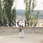 a couple facing each other at Bench 1775 Winery, naramata with the winery name in the background